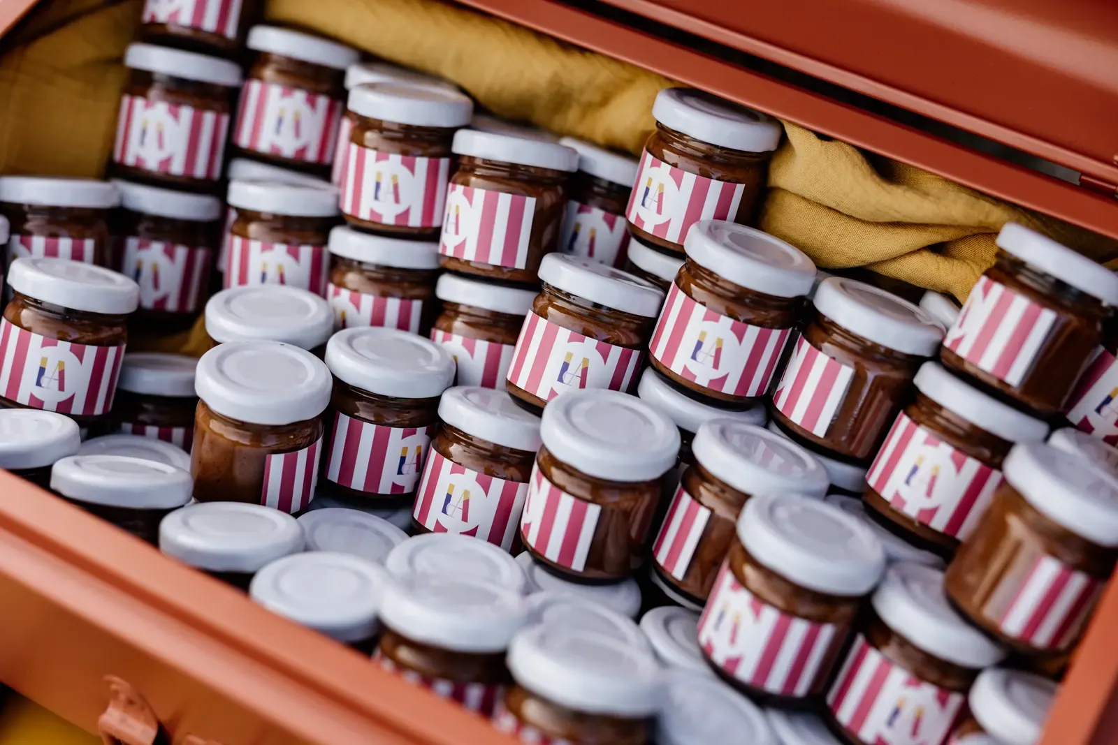 Rows of jars packed in the trunk, each labelled with the event monogram on striped paper