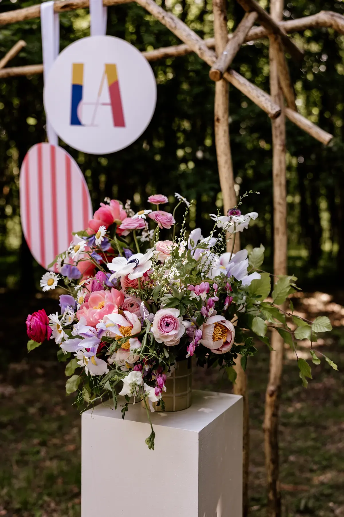 Monogram disc and a striped disc hanging from the ceremony arch above a floral pedestal
