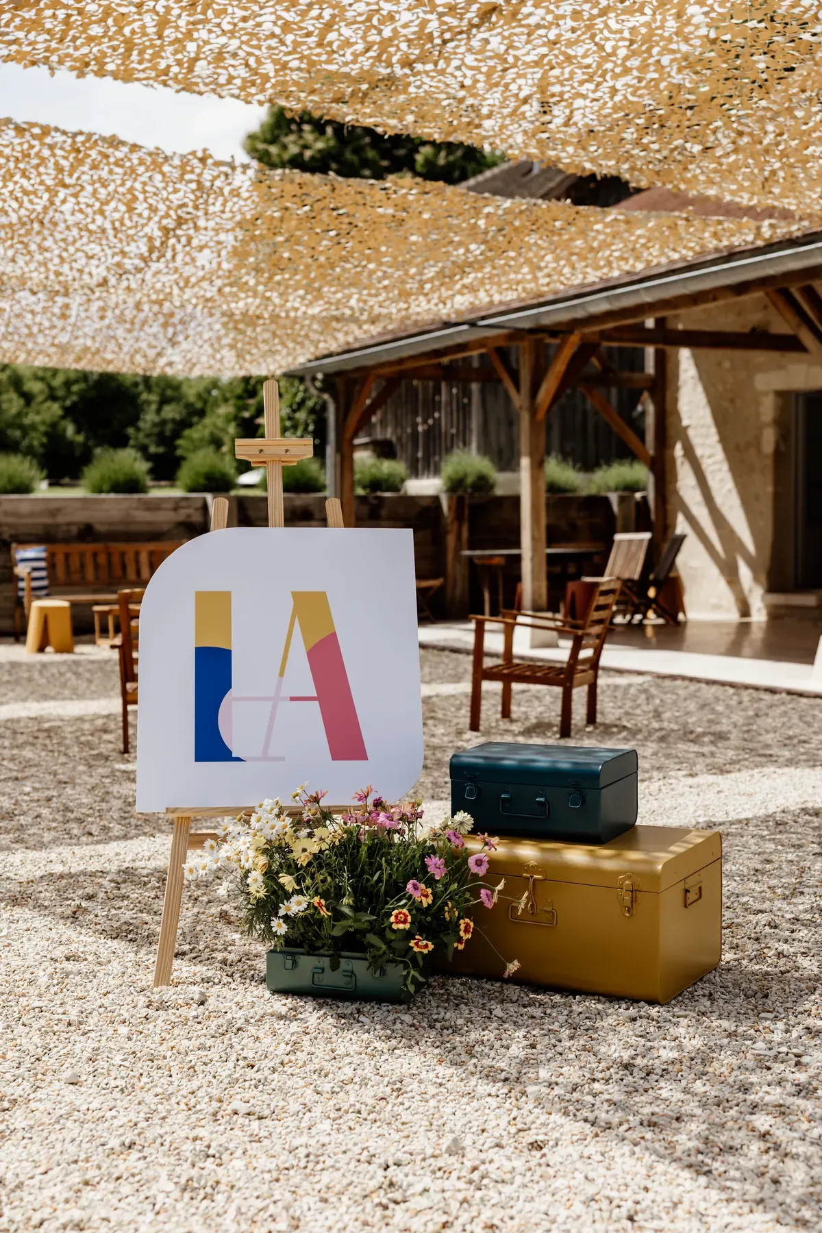 Welcome sign on an easel showing the event monogram, beside stacked metal trunks