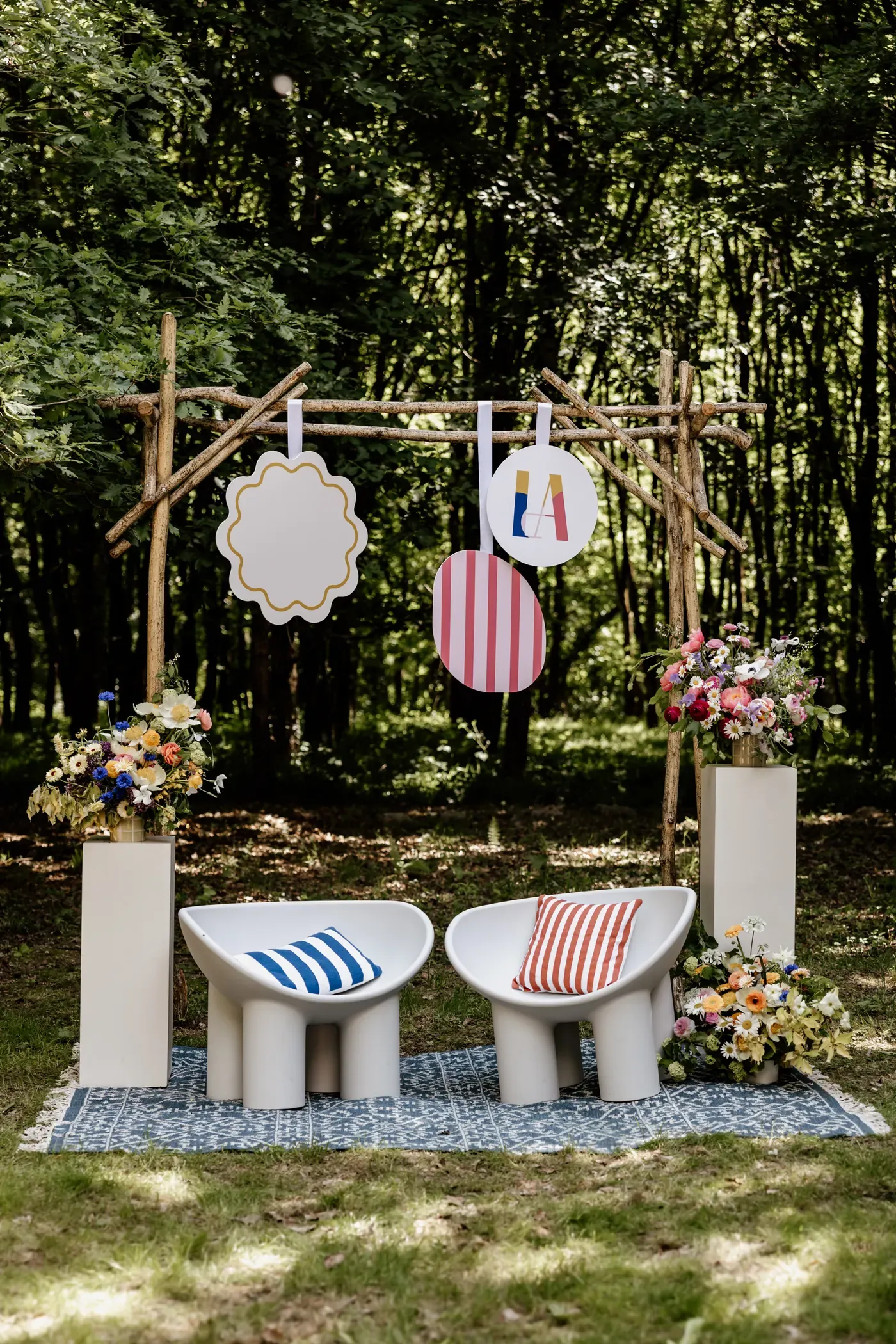Ceremony arch hung with shapes from the event's visual identity, framed by floral pedestals and two seats