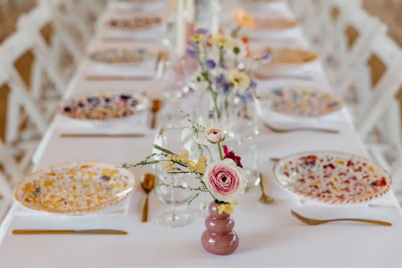 Long table with patterned plates, gold cutlery and single-stem vases running down the centre