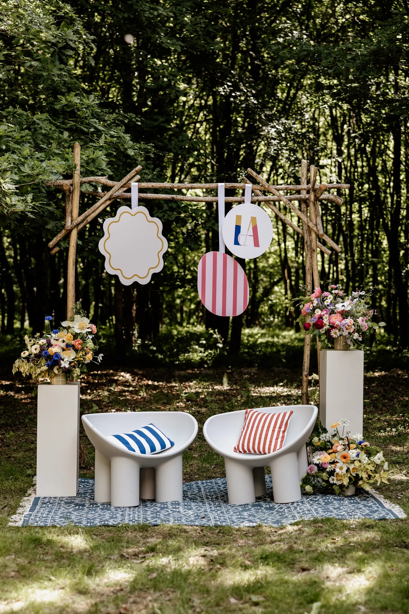 Ceremony arch hung with shapes from the event's visual identity, framed by floral pedestals and two seats