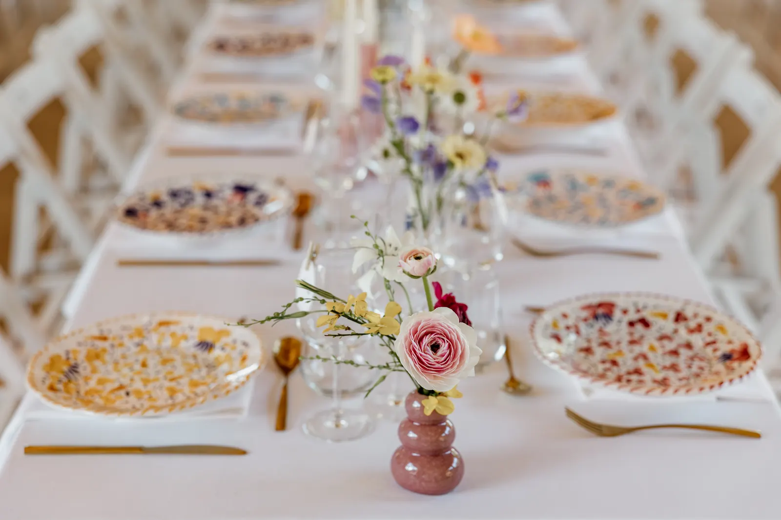 Long table with patterned plates, gold cutlery and single-stem vases running down the centre